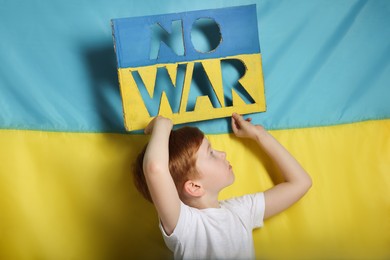 Photo of Boy holding poster No War against Ukrainian flag