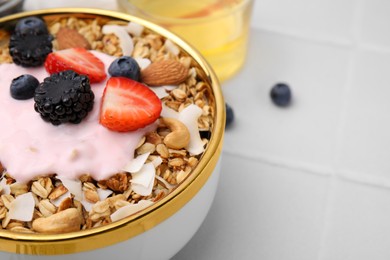 Tasty granola, yogurt and fresh berries in bowl on white tiled table, closeup with space for text. Healthy breakfast
