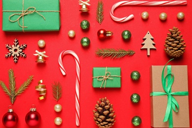 Photo of Christmas tree branches and festive decoration on red background, flat lay