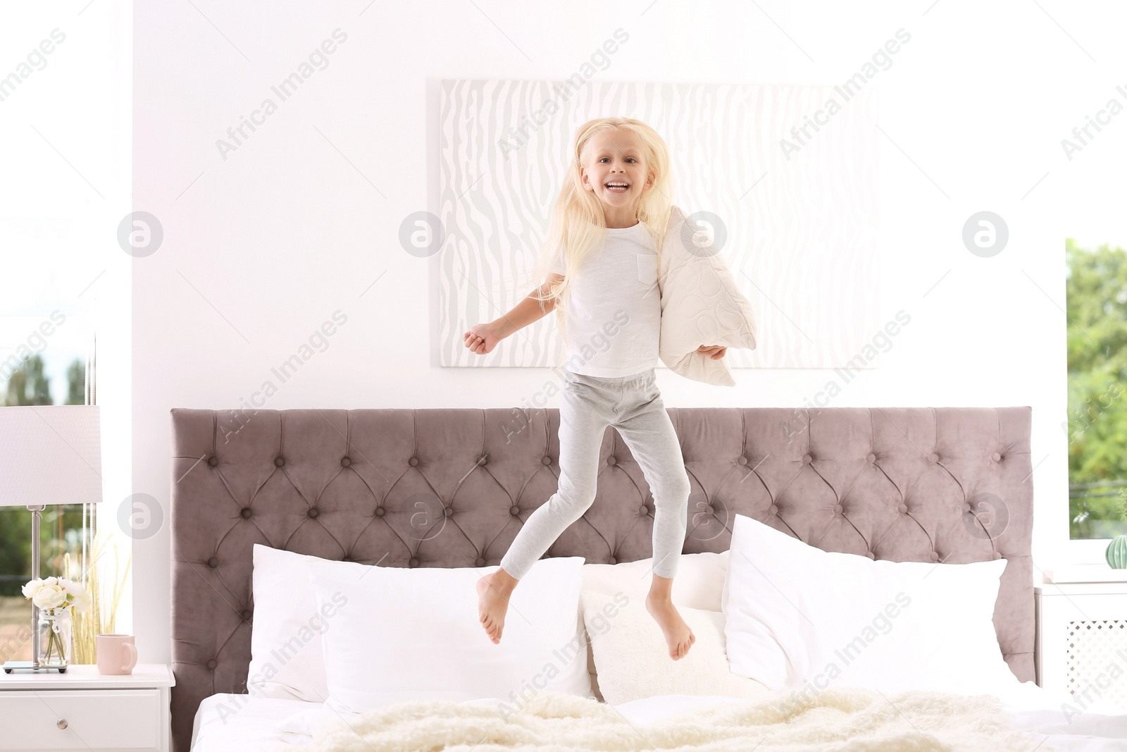 Photo of Cute little girl with pillow jumping on bed at home