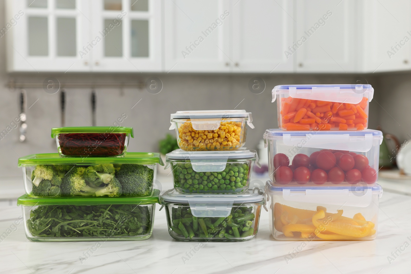 Photo of Glass and plastic containers with different fresh products on white marble table in kitchen. Food storage