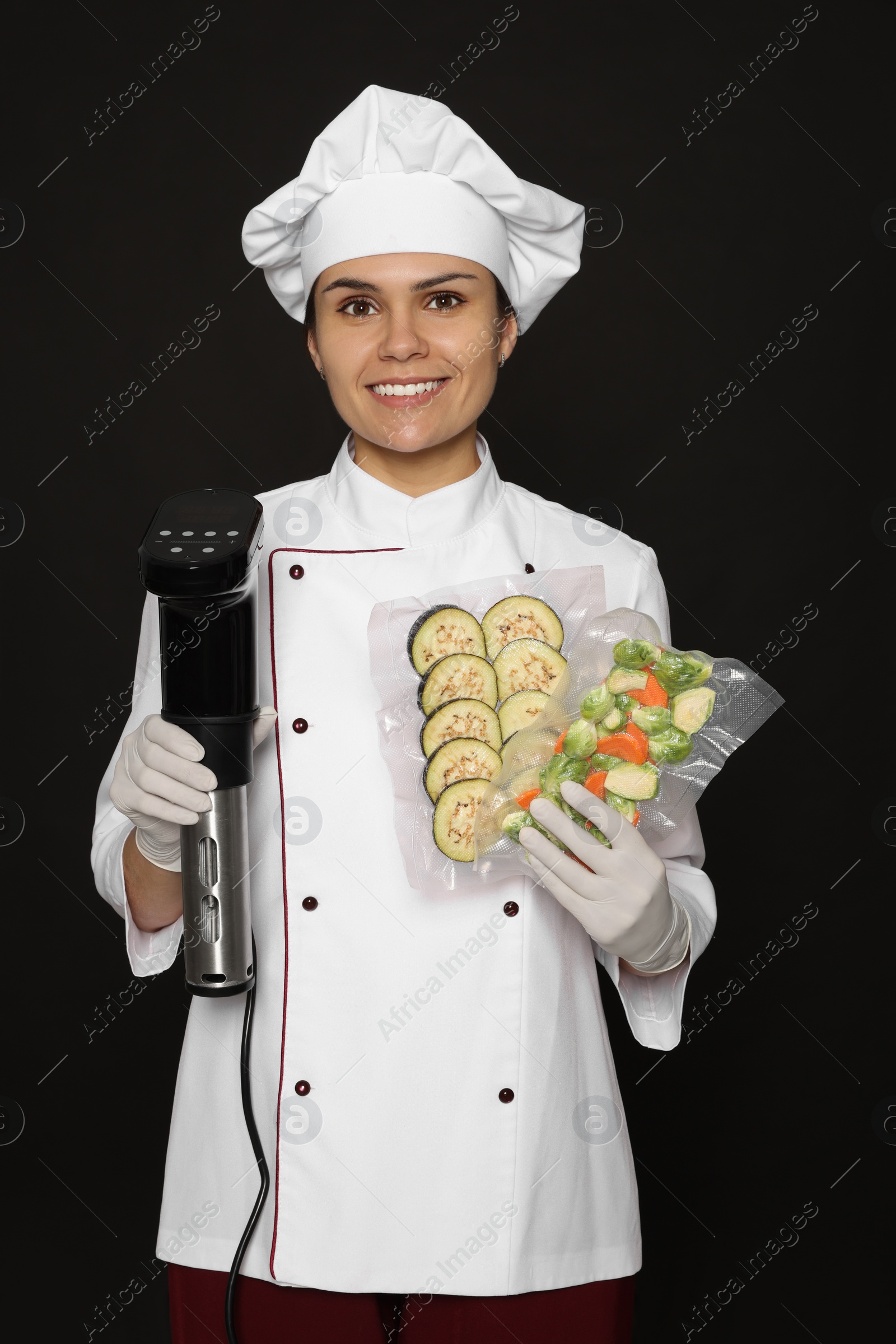 Photo of Chef holding sous vide cooker and vegetables in vacuum packs on black background