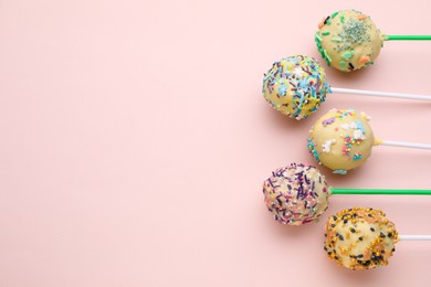 Photo of Delicious confectionery. Sweet cake pops decorated with sprinkles on pale pink background, flat lay. Space for text