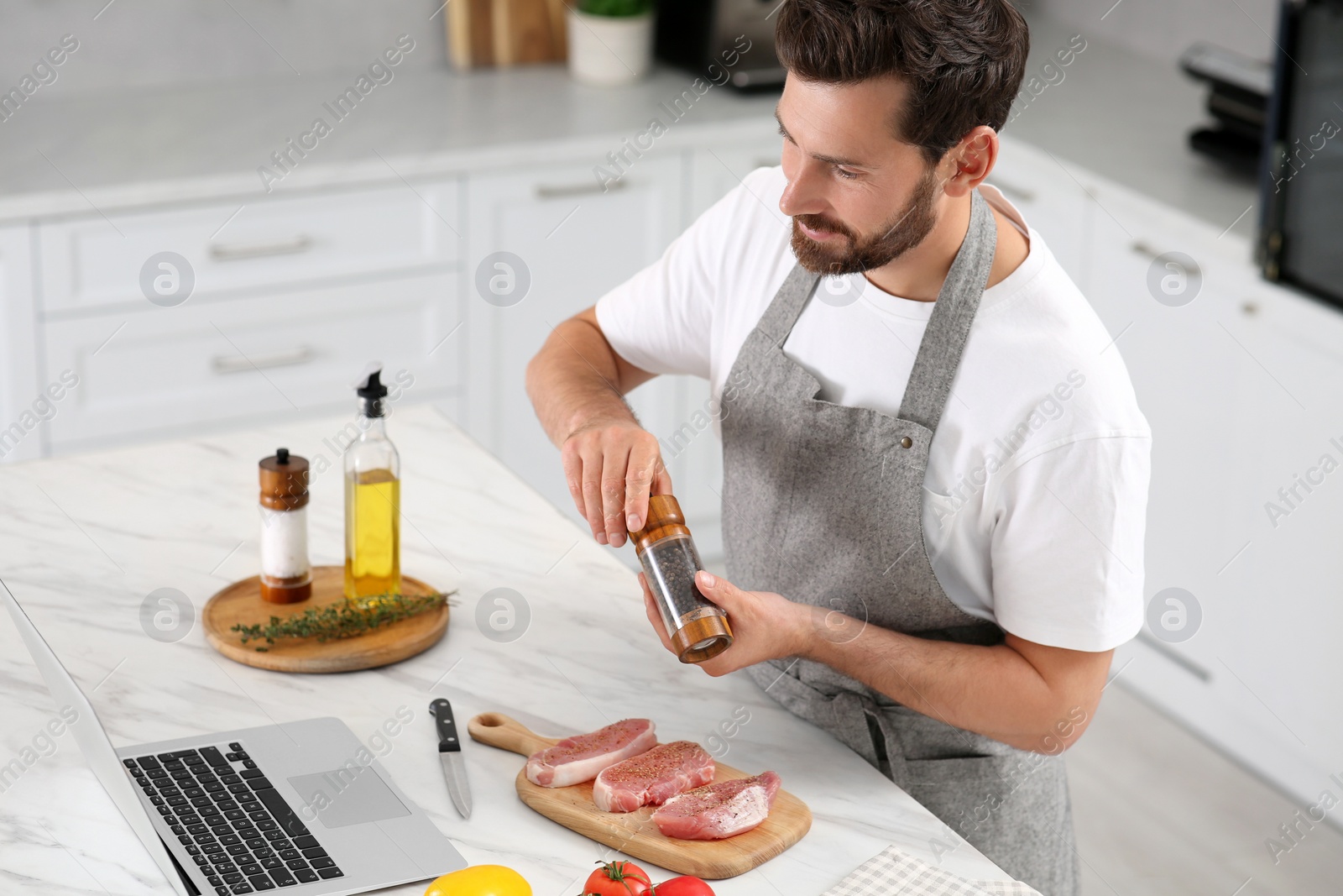 Photo of Man making dinner while watching online cooking course via laptop in kitchen