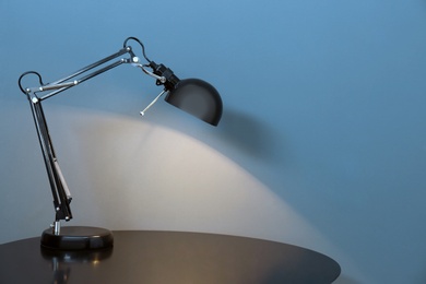 Modern lamp on table against color background. Space for text