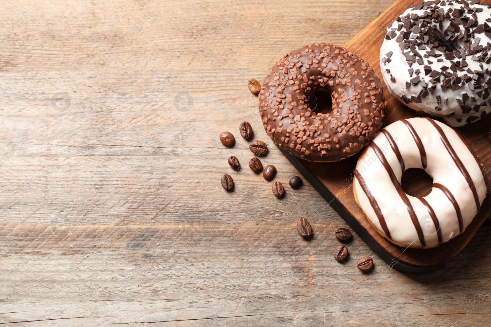 Photo of Yummy donuts with sprinkles on wooden table, flat lay. Space for text