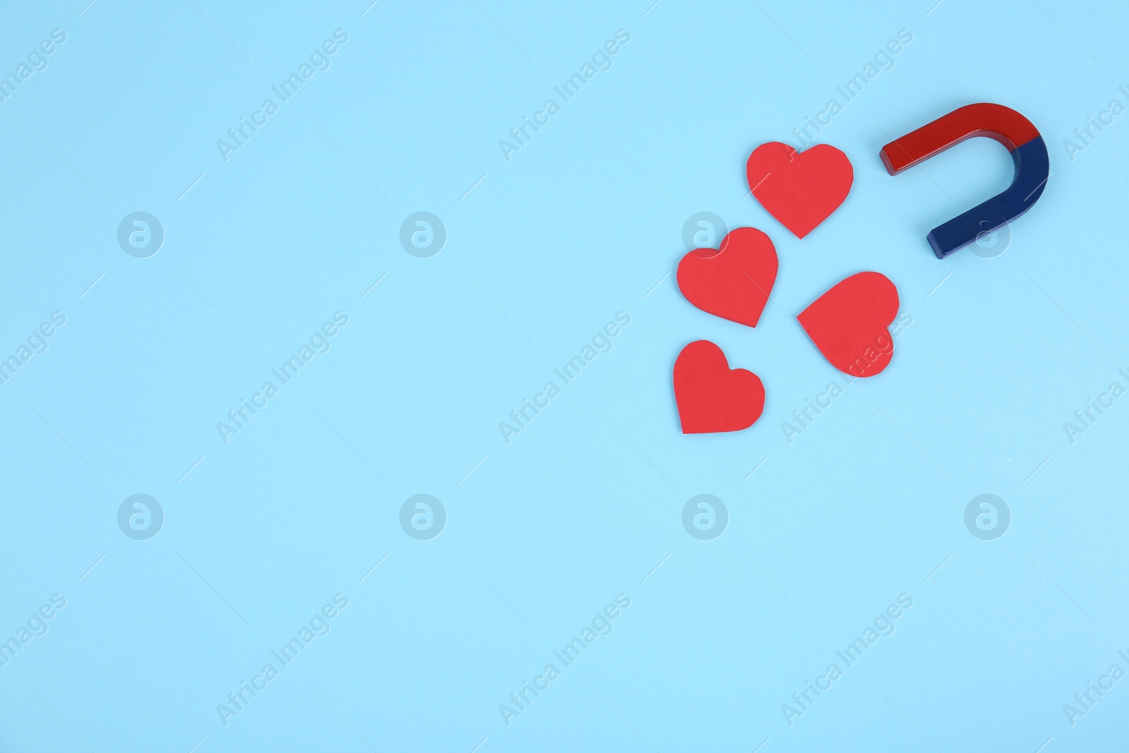 Photo of Magnet attracting hearts on light blue background, flat lay. Space for text
