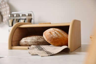 Wooden bread basket with freshly baked loaves on white marble table in kitchen