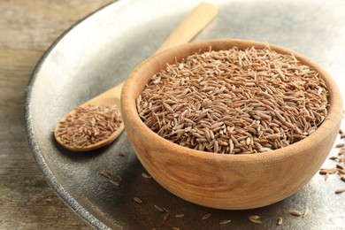 Photo of Bowl of caraway seeds and spoon on wooden table, closeup
