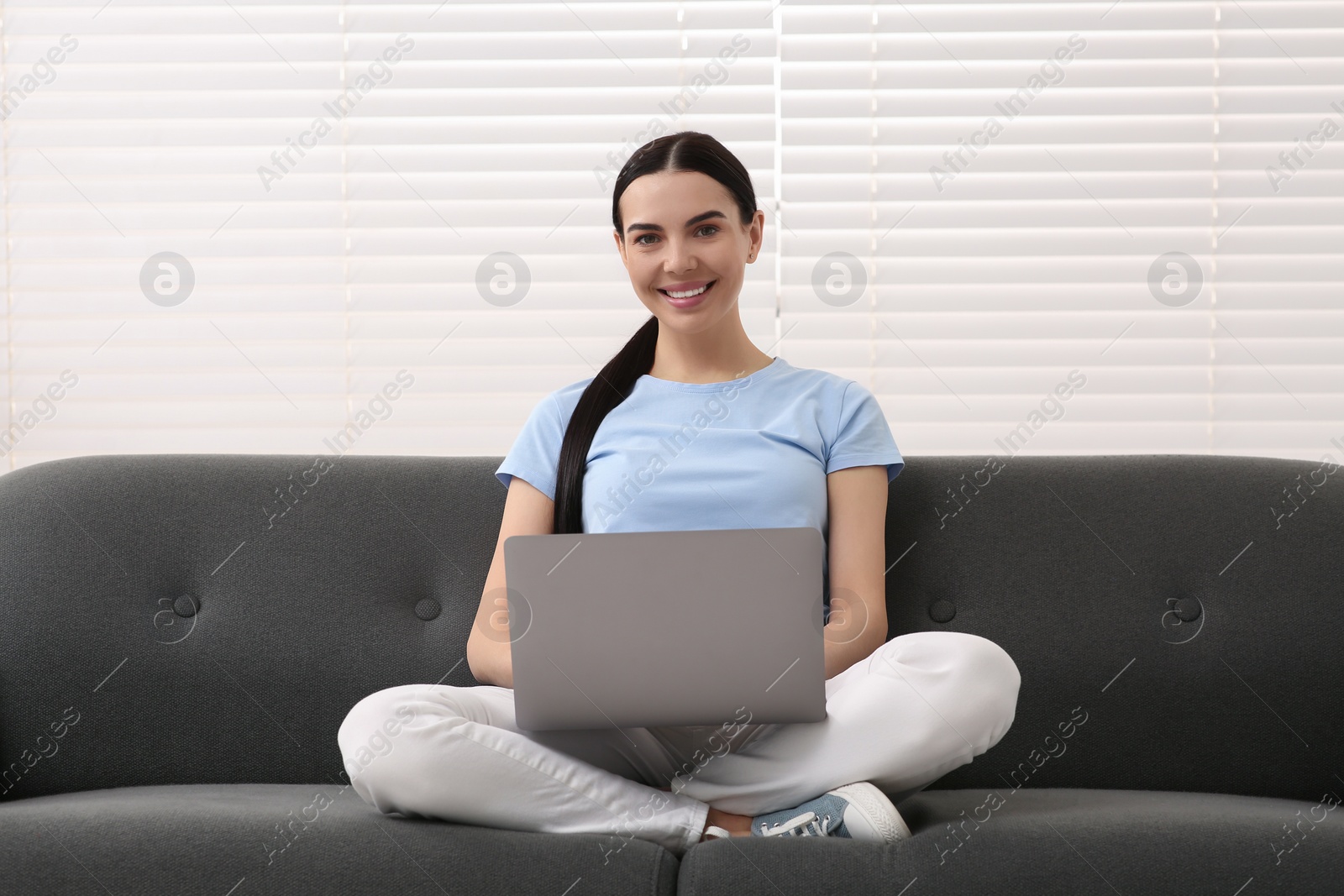 Photo of Happy woman working with laptop on sofa indoors