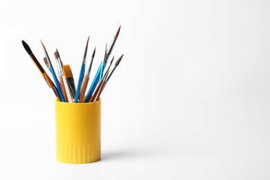 Photo of Holder with different paint brushes on white background. Space for text