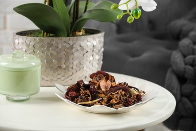 Aromatic potpourri of dried flowers in plate and beautiful houseplant on white table indoors