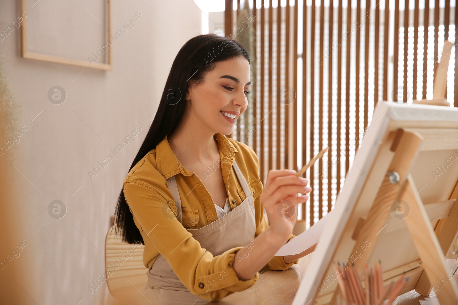 Photo of Young woman drawing on easel with pencil at table indoors