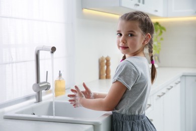 Photo of Cute little girl washing hands with liquid soap in kitchen