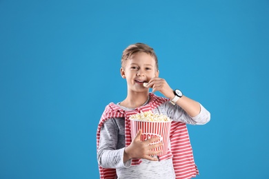 Cute boy with popcorn bucket on color background