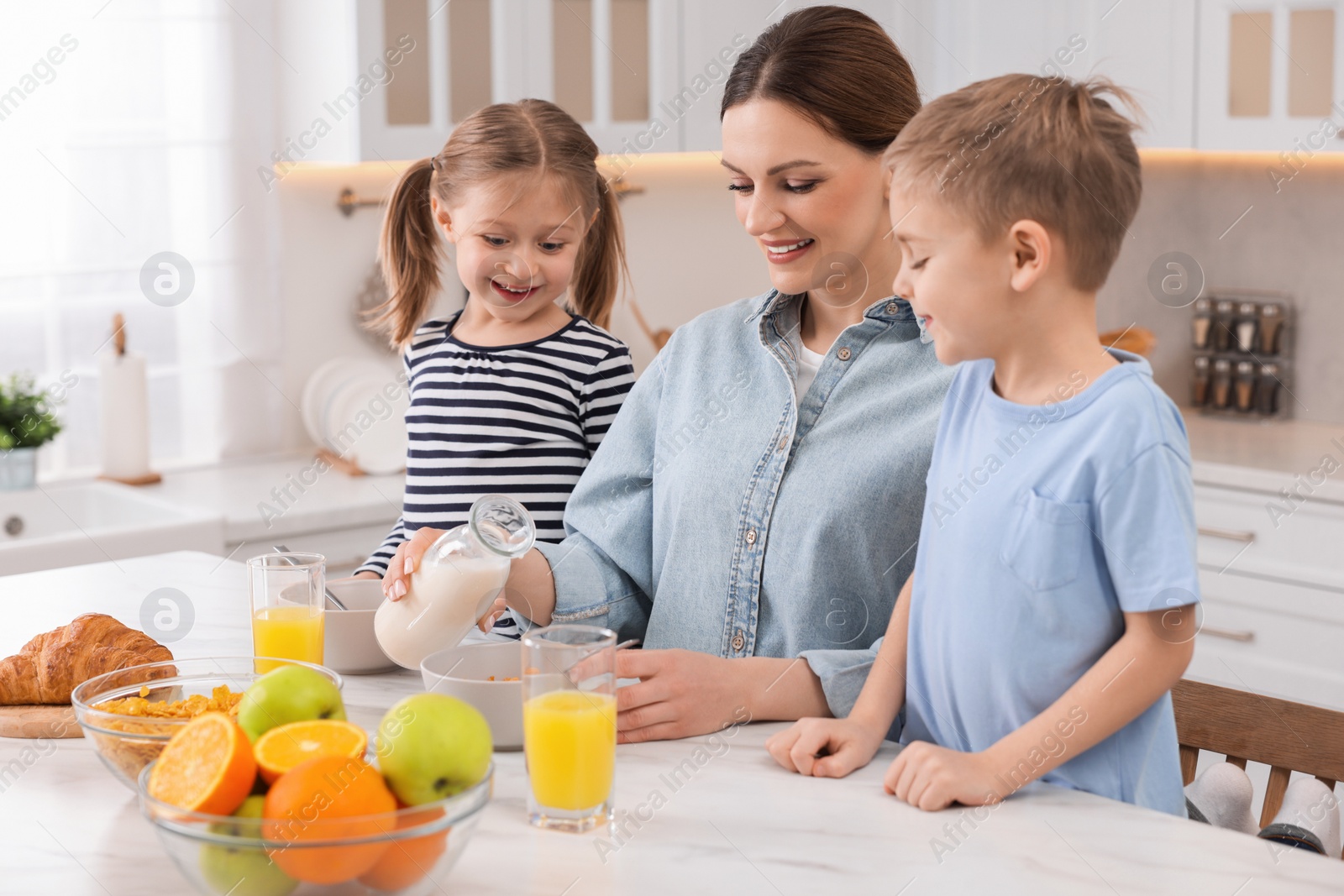 Photo of Mother and her little children having breakfast at table in kitchen