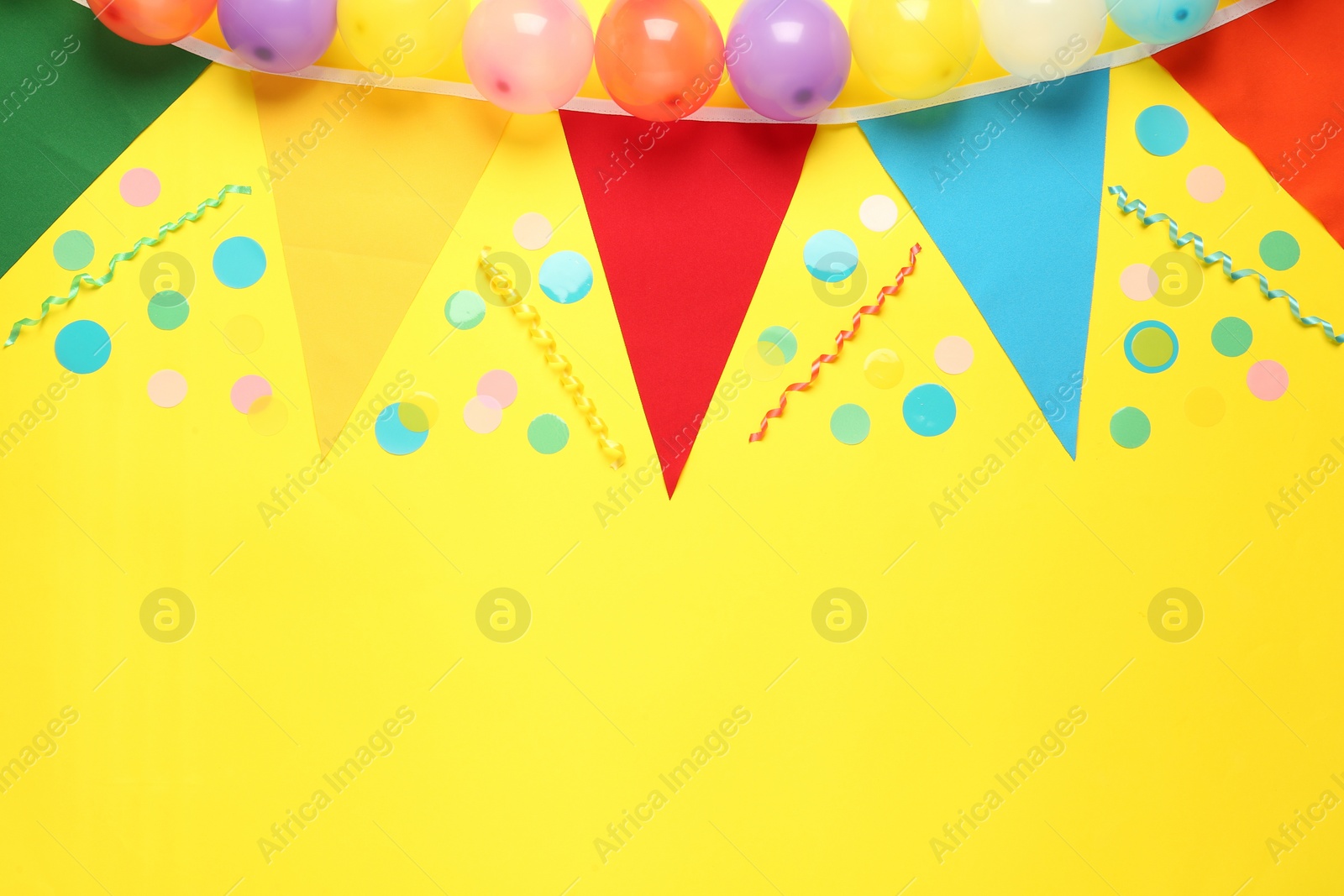 Photo of Bunting with colorful triangular flags and other festive decor on yellow background, flat lay. Space for text