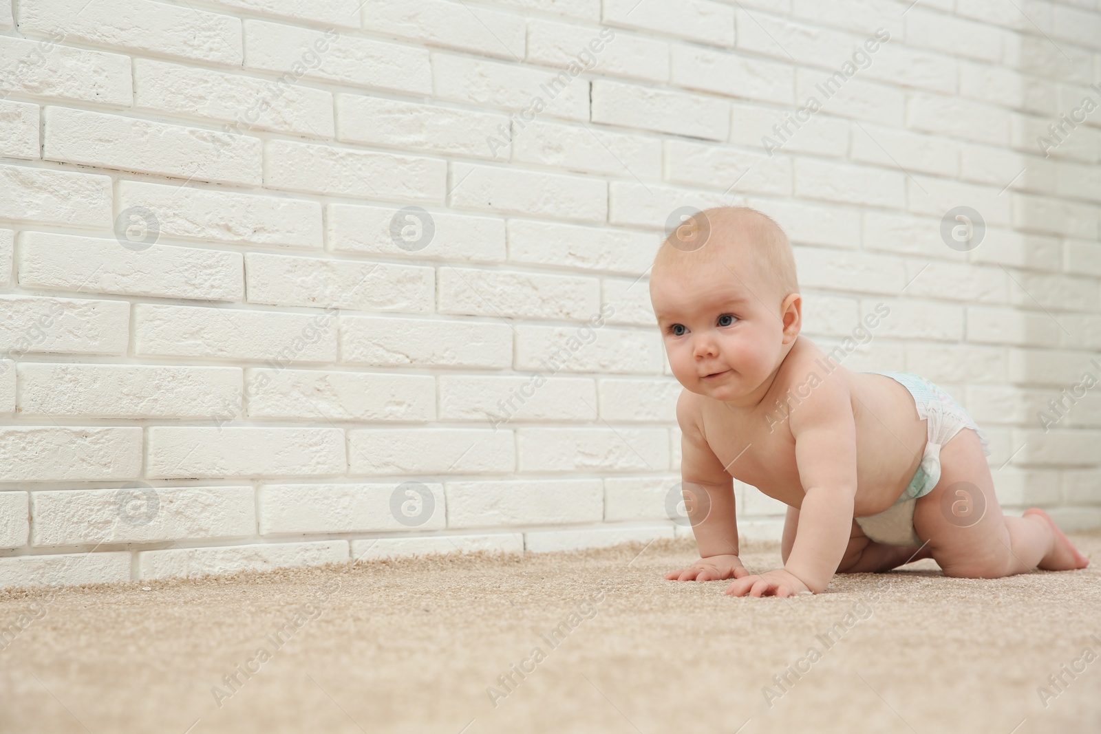 Photo of Cute little baby crawling on carpet near brick wall, space for text