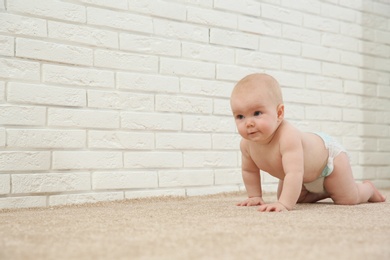 Cute little baby crawling on carpet near brick wall, space for text