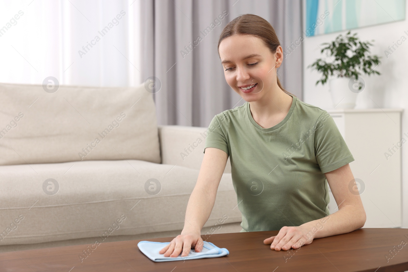 Photo of Woman with microfiber cloth cleaning wooden table in room