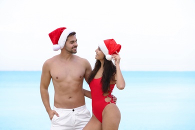 Happy young couple with Santa hats together on beach