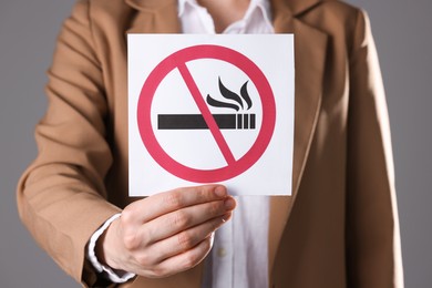 Photo of Woman holding card with no smoking sign on gray background, closeup