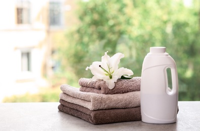 Photo of Stack of clean towels with lily and detergent on table against blurred background. Space for text