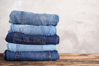 Stack of different jeans on wooden table. Space for text