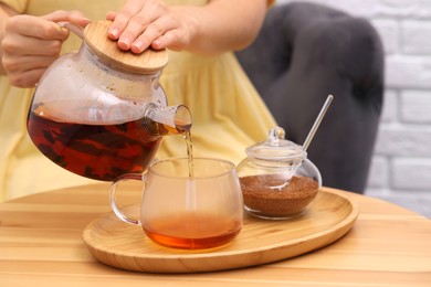 Photo of Woman pouring aromatic hot tea into glass cup at wooden table, closeup