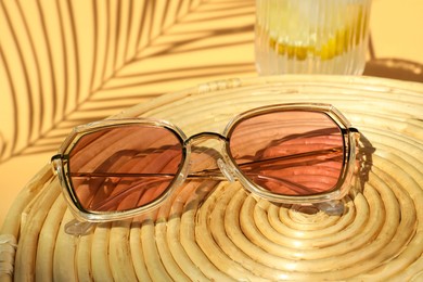 Photo of Stylish sunglasses on wicker mat against beige background, closeup