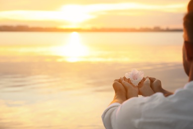 Couple holding beautiful flower near river at sunset, closeup view with space for text. Nature healing power