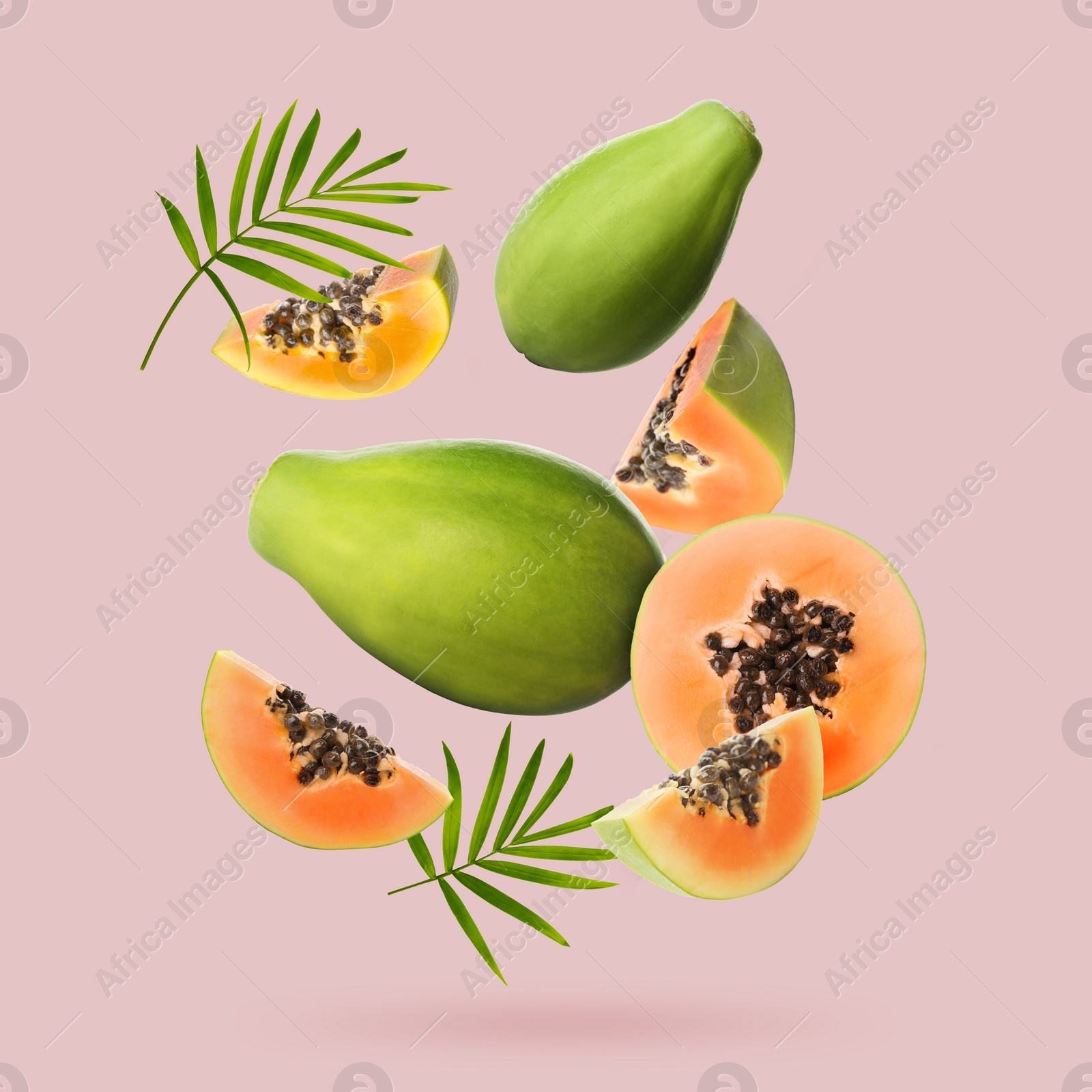 Image of Fresh papaya fruits and green leaves falling on dusty pink background