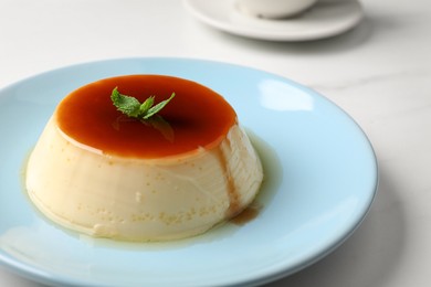 Photo of Delicious pudding with caramel and mint on white table, closeup