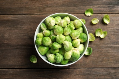 Photo of Bowl of fresh Brussels sprouts and leaves on wooden background, top view