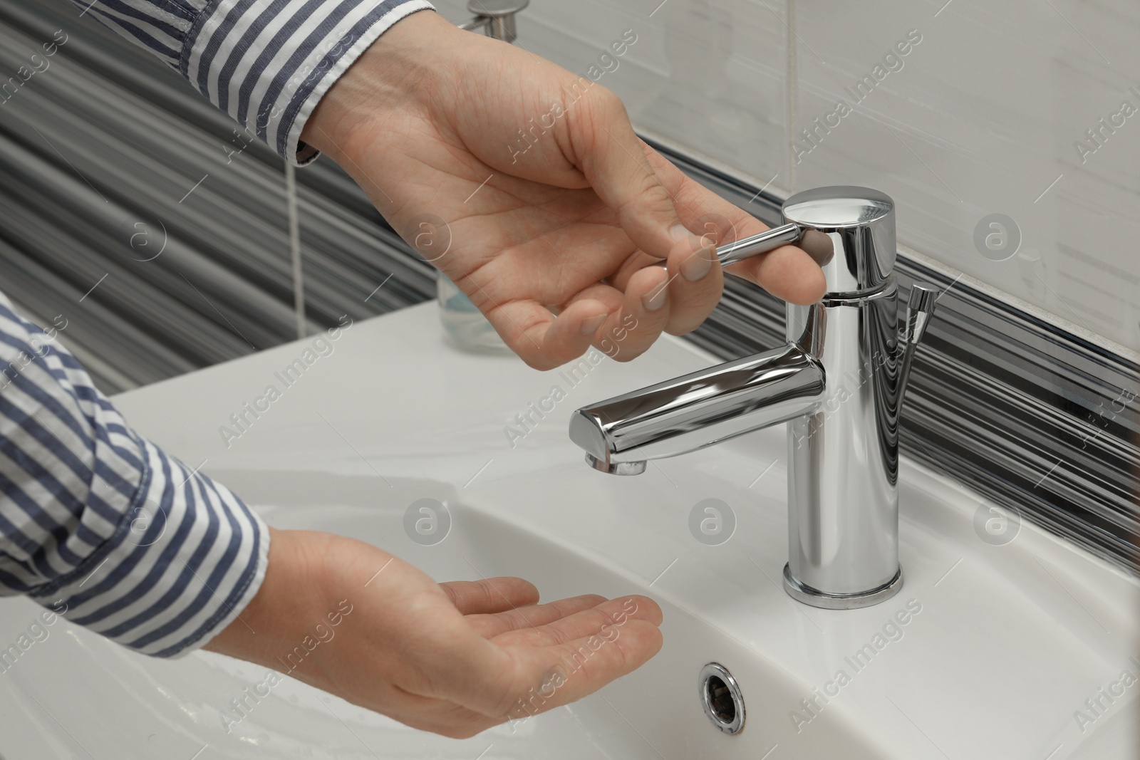 Photo of Man using water tap to wash hands in bathroom, closeup