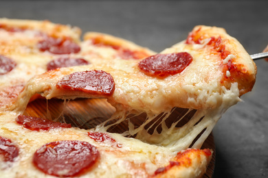 Photo of Taking slice of tasty pepperoni pizza on table, closeup