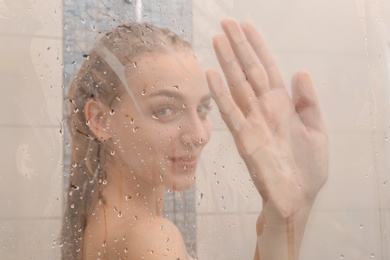 Photo of Young woman taking shower, view through glass door