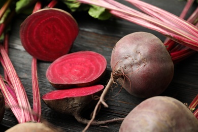 Photo of Cut and whole raw beets on wooden table, closeup