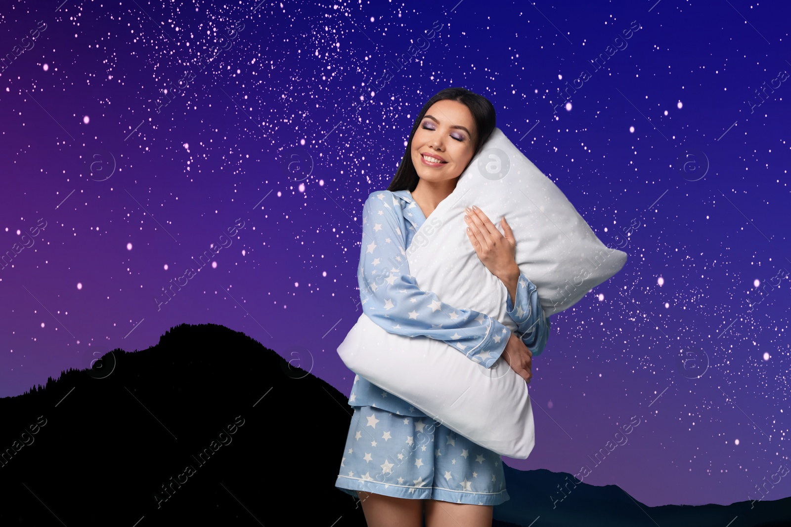 Image of Beautiful woman with pillow, mountains under starry sky on background. Bedtime