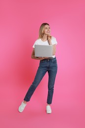 Young woman with modern laptop on pink background