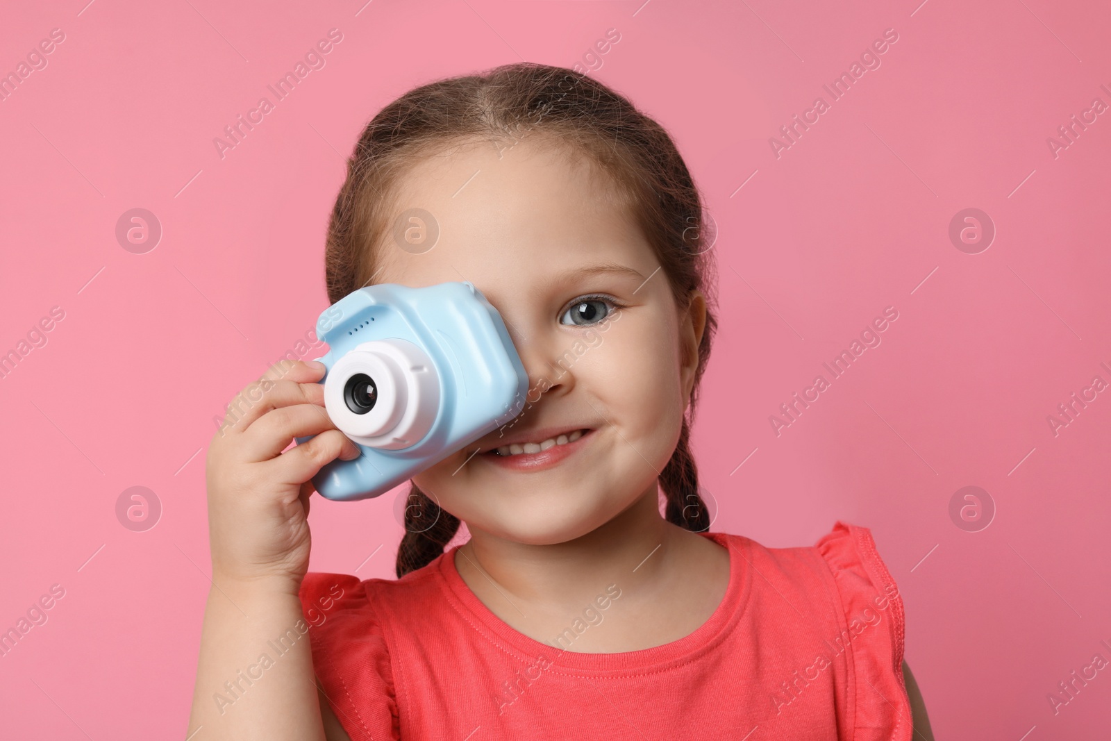 Photo of Little photographer taking picture with toy camera on pink background