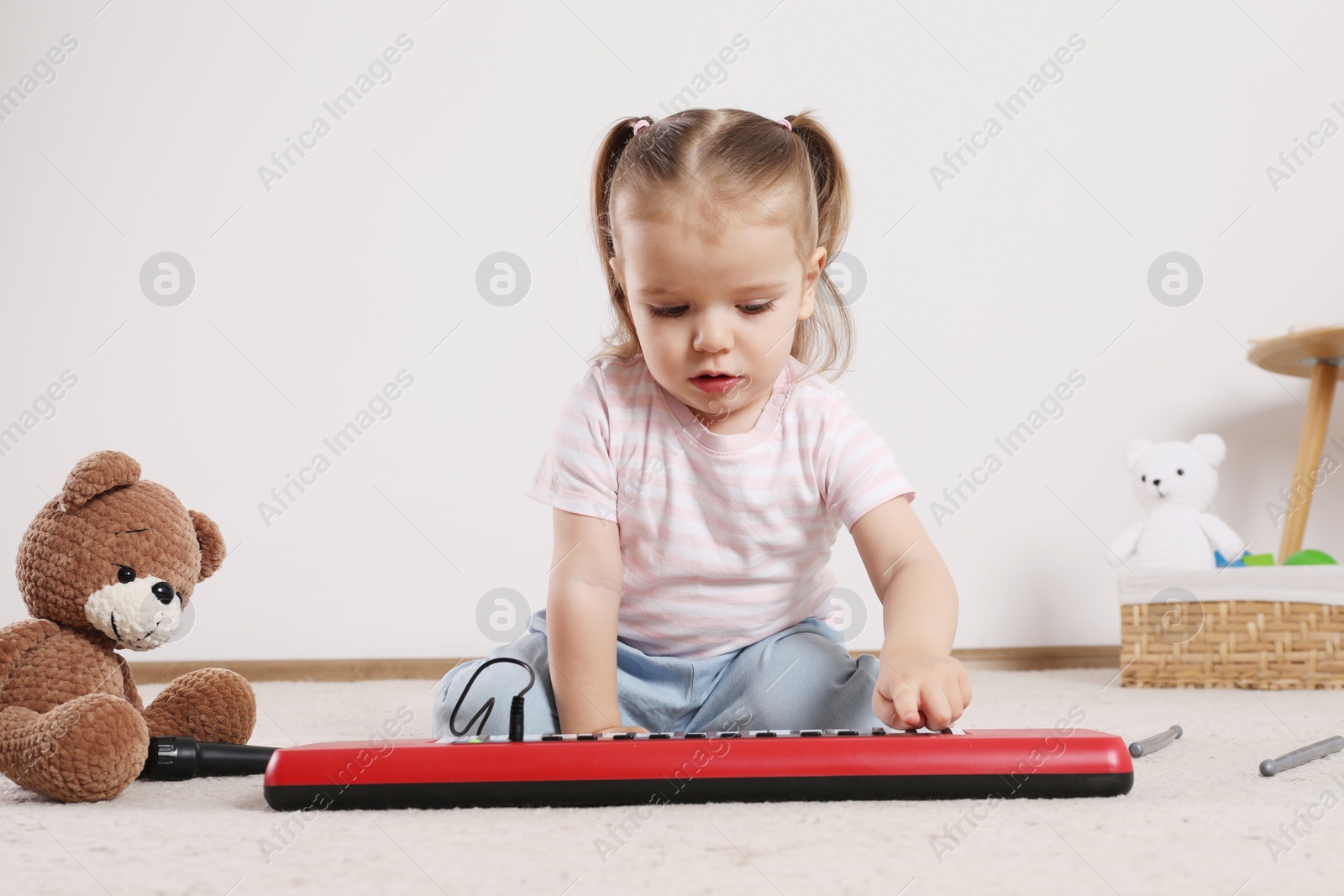 Photo of Cute little girl playing with toy piano at home