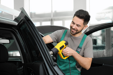 Worker tinting car window with heat gun in workshop