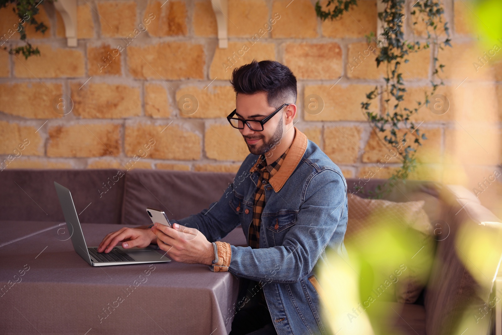 Photo of Young blogger with laptop and phone at table in cafe