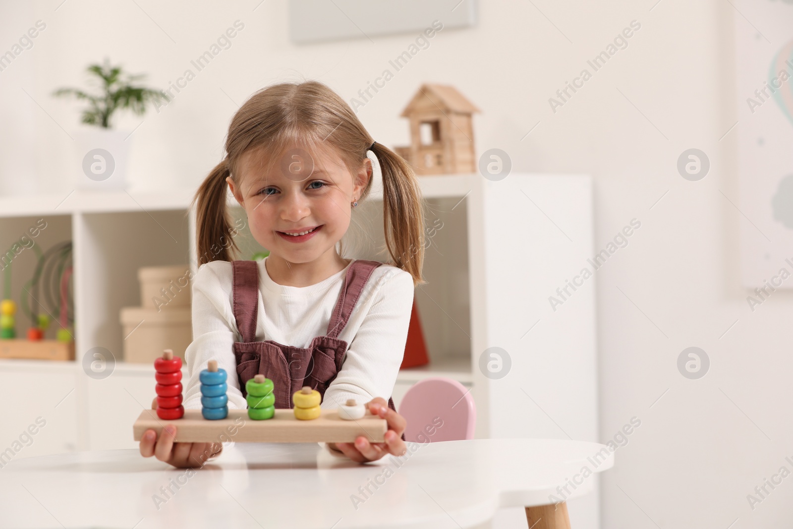 Photo of Cute little girl playing with stacking and counting game at white table indoors, space for text. Child's toy