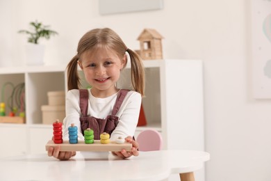 Cute little girl playing with stacking and counting game at white table indoors, space for text. Child's toy