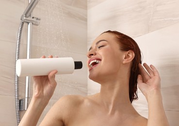 Washing hair. Happy young woman with bottle of shampoo singing in shower