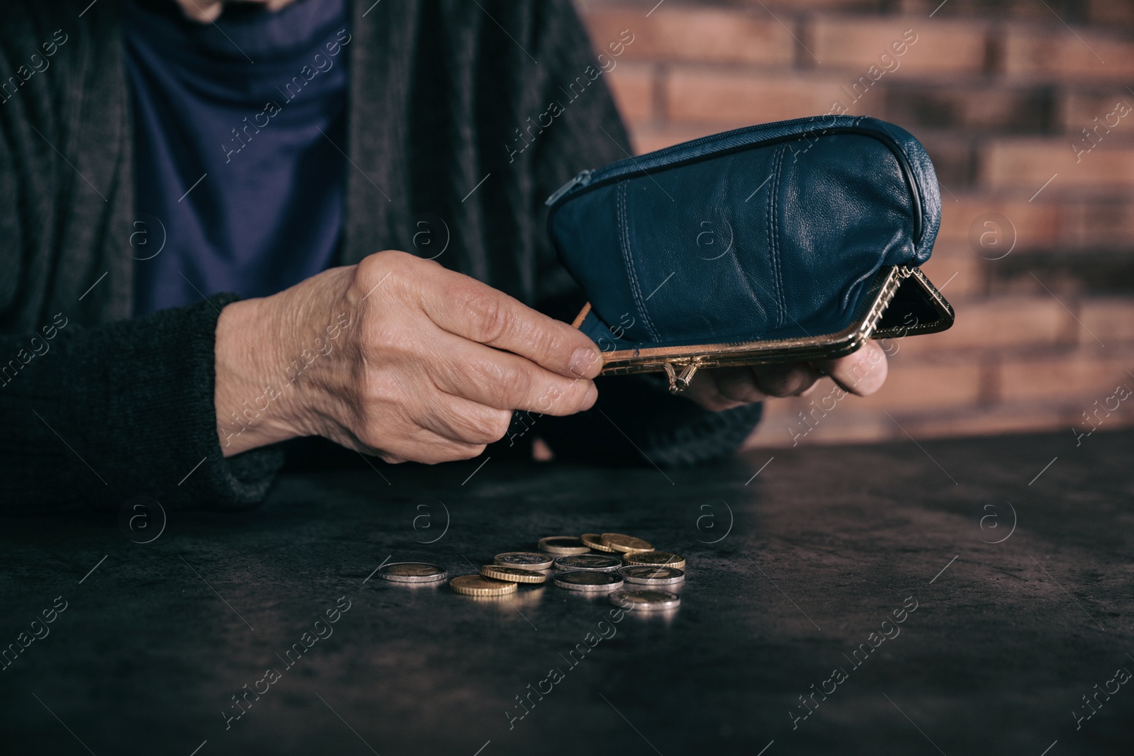 Photo of Poor mature woman pouring coins out of wallet at table, closeup