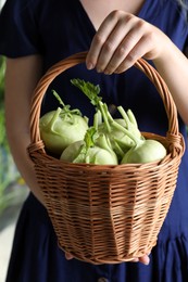 Photo of Woman holding wicker basket with ripe kohlrabi plants outdoors, closeup