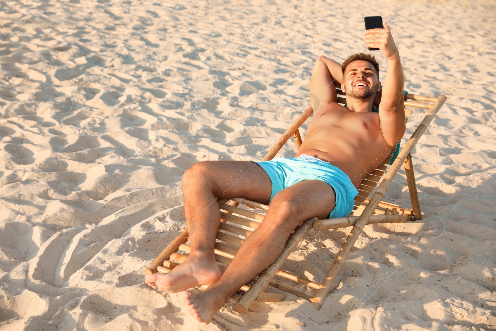 Photo of Young man taking selfie in deck chair on beach